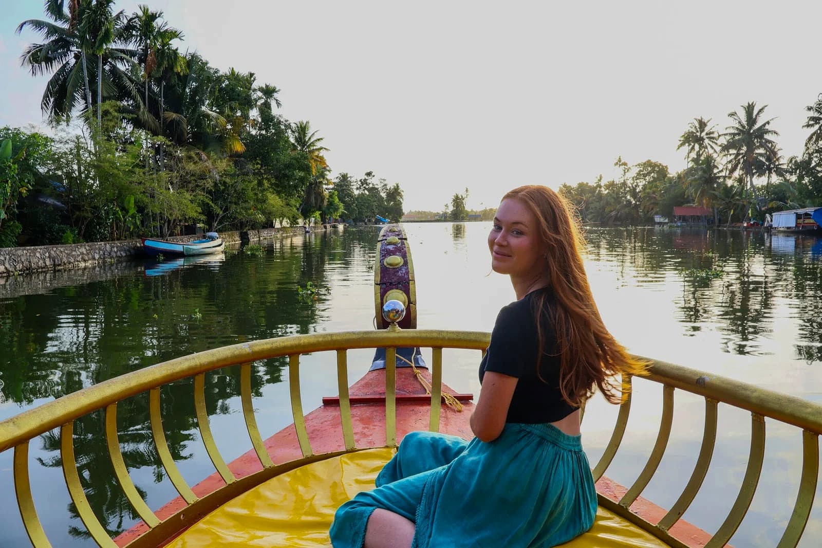 Traveler relaxing on the front bow of a traditional shikara boat at golden hour on Punnamada Lake in Alleppey